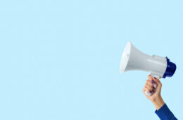 Megaphone in woman hand on blue background. Creative announcement concept.